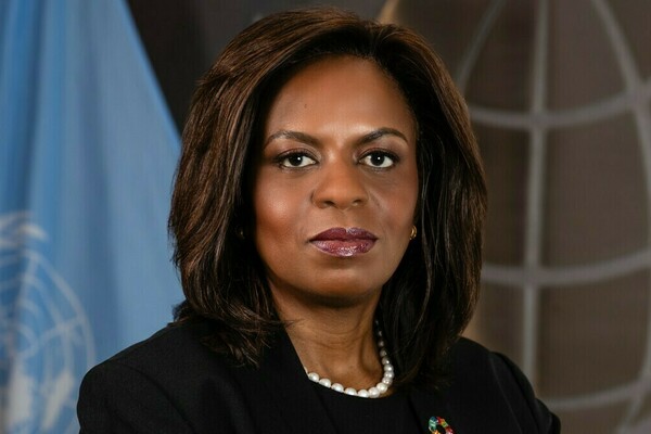 Sanda Ojiambo stands in front of a UN flag and looks at the camera